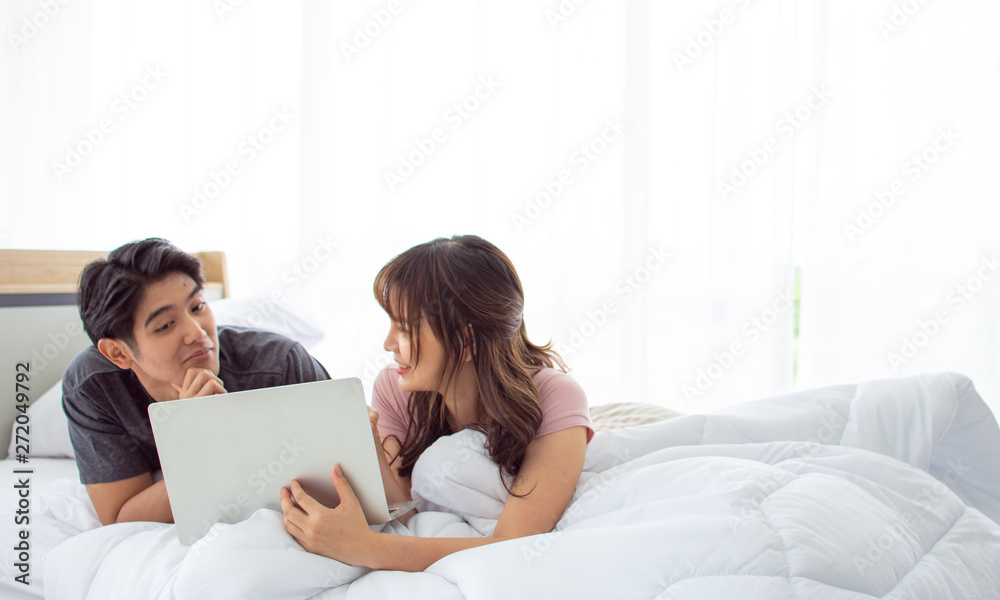 A cute couple is using laptop together in the bedroom A cute couple is using laptop together in the bedroom