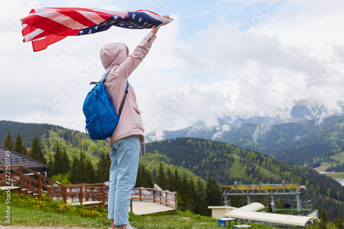 Full length profile shot of beautiful young woman with American flag held in her outstretched hand standing in front of tourist base, distant mountains and sky. Traveling, active vocation concept. photo