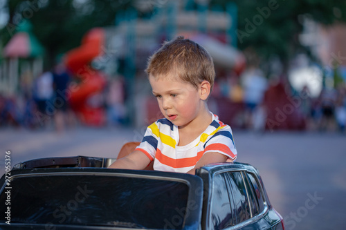 Amusement Park, a funny boy rides on a toy electric car on a sunny summer day, finish marking © Delete