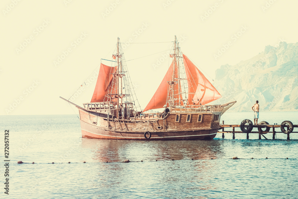 A ship with red sails at sea pier on the background of mountains A ship with red sails at sea pier on the background of mountains