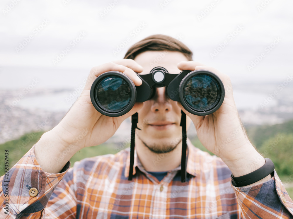 Traveler young man looking through binoculars outdoor, front view. - obrazy, fototapety, plakaty 