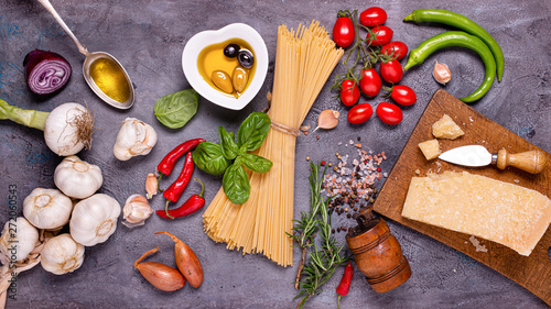top view, on a dark gray rustic background, Italian spaghetti with olive oil, seasoned cheese, bunch of tomatoes, various vegetables and spices