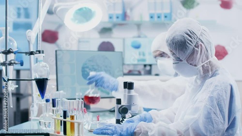 Chemist giving a test sample to her colleague to look ai it under the microscope