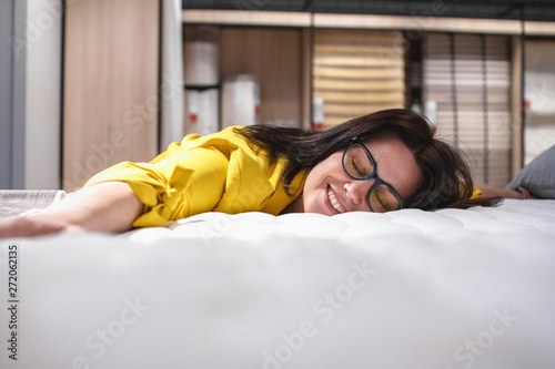 A beautiful girl is testing a new mattress before buying. Portrait of a satisfied brunette lying on a new bed. The concept of Healthy sleep photo