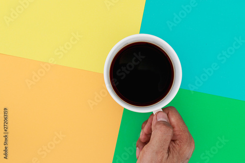 Hands holding the coffee cup hot on a brightly colored background. Top view.