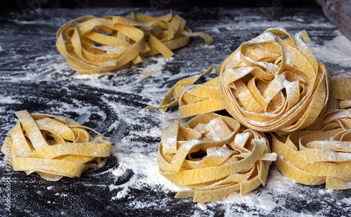 Homemade uncooked pasta on black background. Making fresh italian fettuccine.