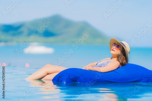 Portrait beautiful young asian woman happy smile relax in swimming pool at hotel resort neary sea ocean beach on blue sky photo