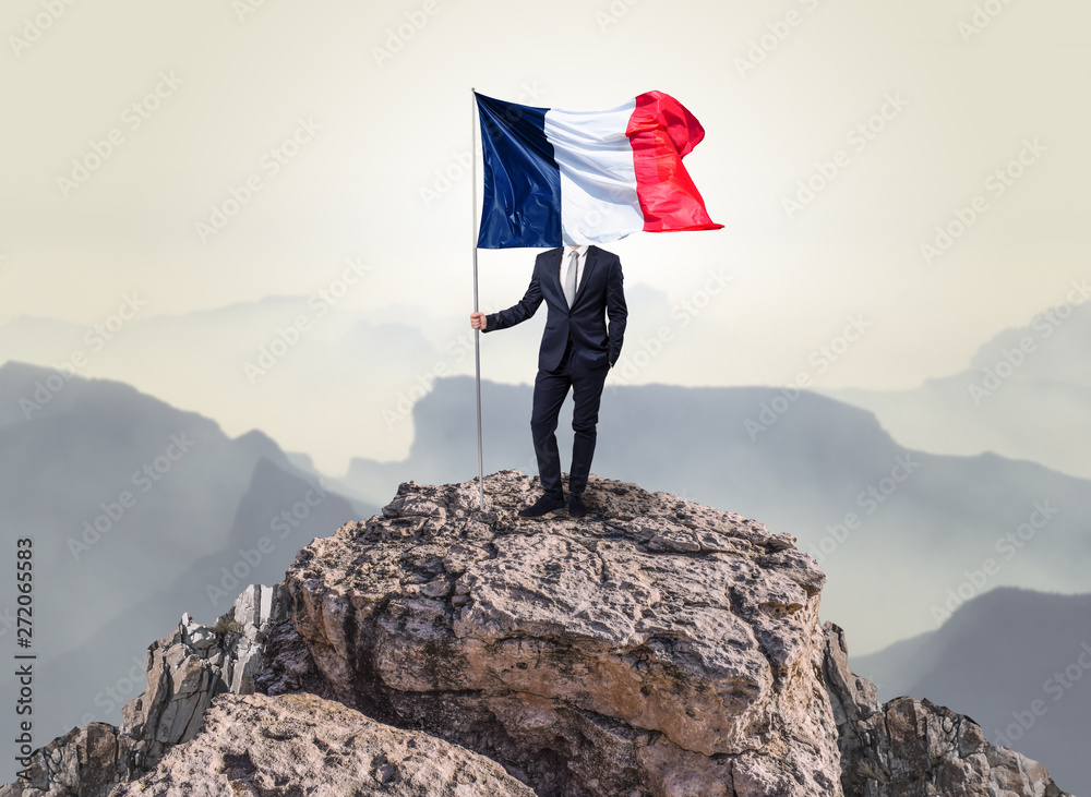 Obraz premium Successful businessman on the top of a mountain holding France victory flag 