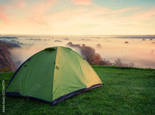 Green tent on hill above misty river