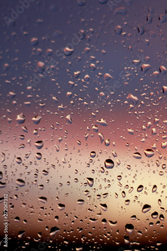 Macro photo of raindrops on glass against a blurred sunset blue violet pink orange red black gradient background. the drops open the sunset