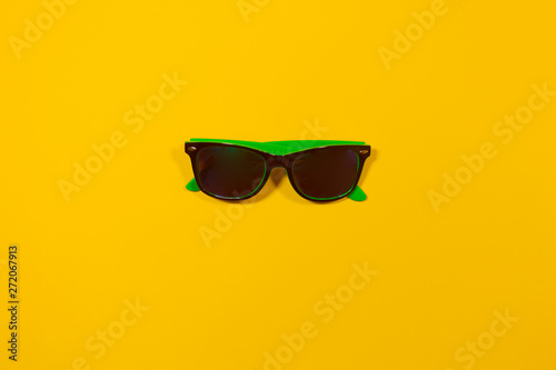 One pair of vacation sunglasses are laying on a yellow surface