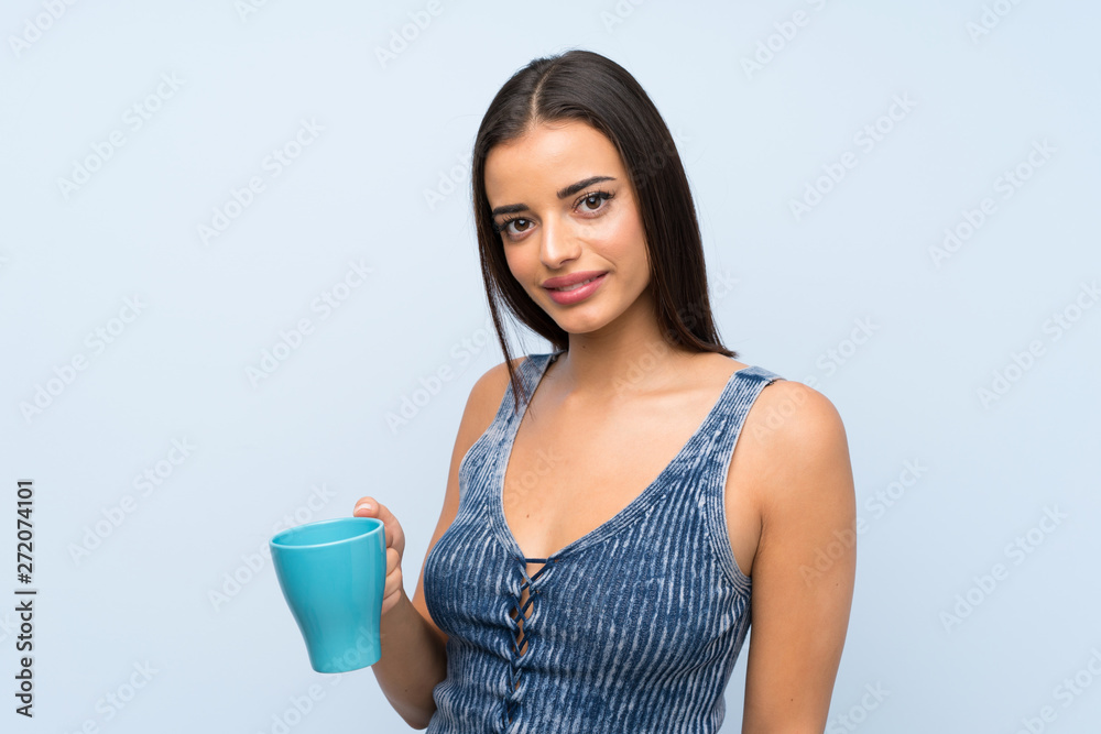 Young woman over isolated blue wall holding hot cup of coffee Young woman over isolated blue wall holding hot cup of coffee