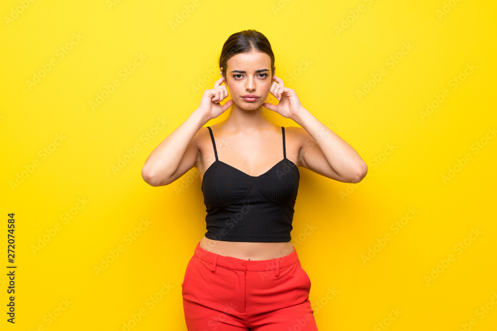 Young woman over isolated yellow background frustrated and covering ears Young woman over isolated yellow background frustrated and covering ears