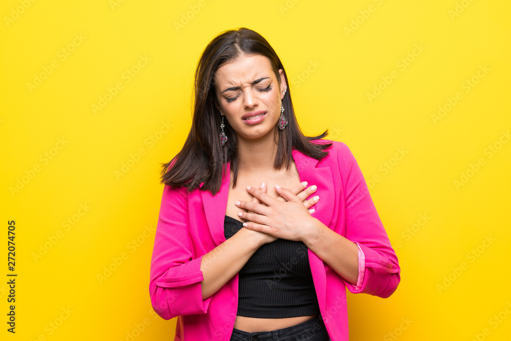 Young woman over isolated yellow background having a pain in the heart Young woman over isolated yellow background having a pain in the heart