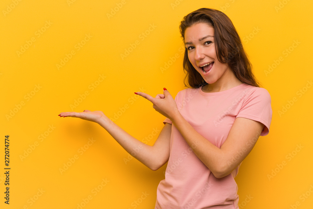 Young european woman isolated over yellow background excited holding a copy space on palm.