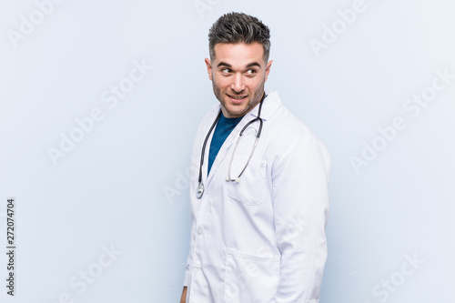 Young handsome doctor man looks aside smiling, cheerful and pleasant.
