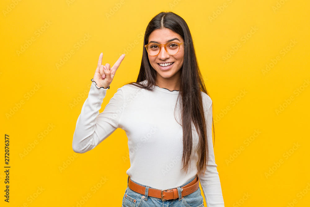 Young pretty arab woman against a yellow background showing a horns gesture as a revolution concept. Young pretty arab woman against a yellow background showing a horns gesture as a revolution concept.