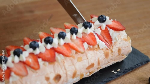 Close up, young girl is cutting meringue roulade with berries and mascarpone. photo