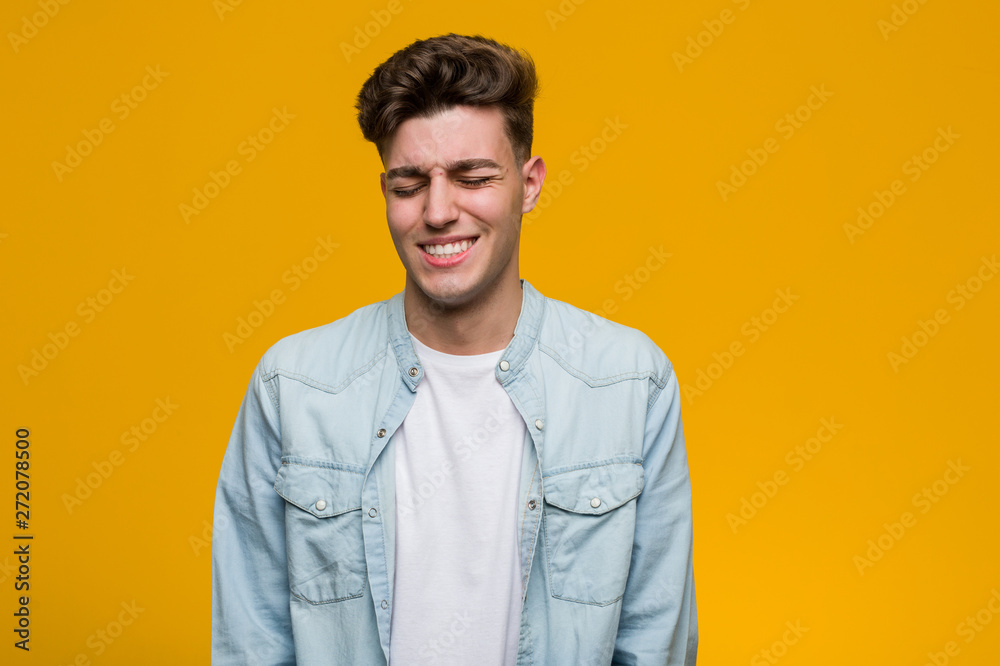 Fototapeta premium Young handsome student wearing a denim shirt laughs and closes eyes, feels relaxed and happy.