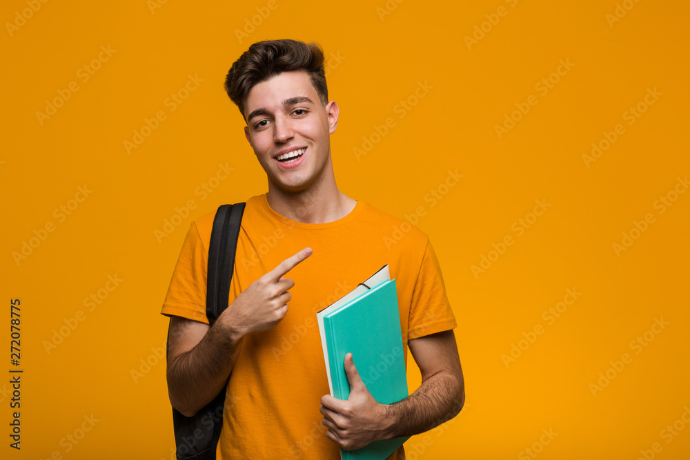 Young student man holding books pointing with finger at you as if inviting come closer. - obrazy, fototapety, plakaty 