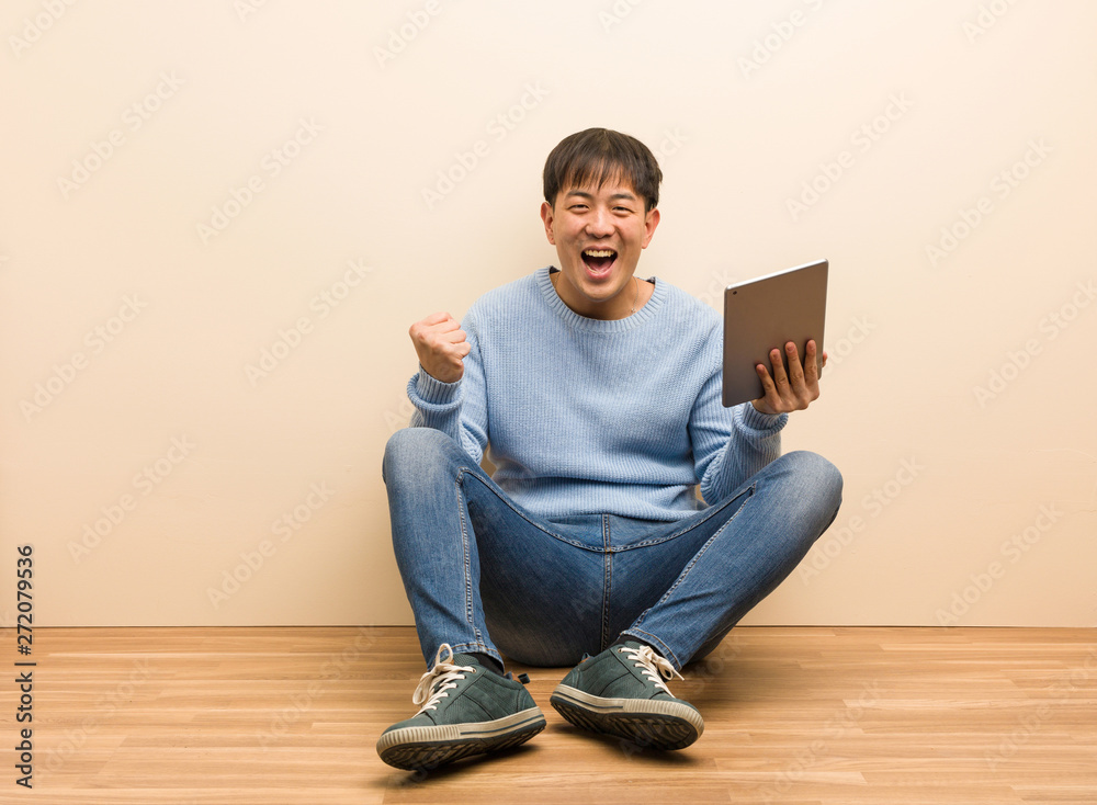 Young chinese man sitting using his tablet surprised and shocked
