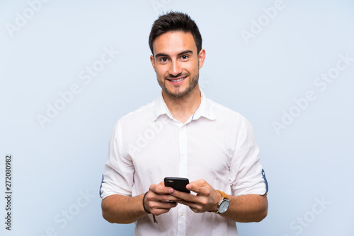 Handsome young man over isolated blue background sending a message with the mobile