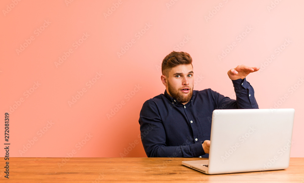 Young man working with his laptop shocked and amazed holding a copy space between hands. Young man working with his laptop shocked and amazed holding a copy space between hands.