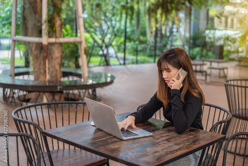 Happy young hipster woman talking on the phone and using tablet computer in at cafe.
