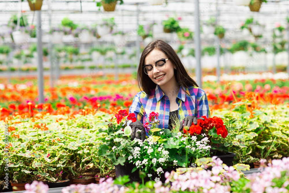 Beautiful young smiling girl in glasses, worker with flowers in greenhouse. Concept work in the greenhouse. Copy space