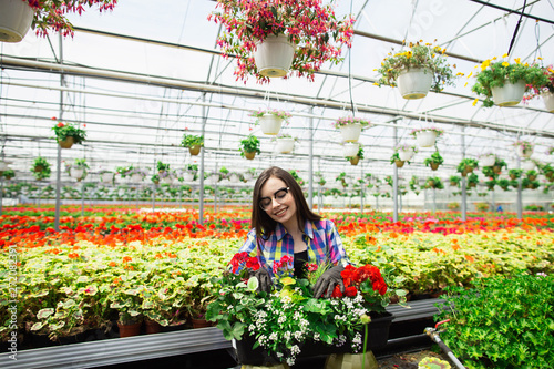 Beautiful young smiling girl in glasses, worker with flowers in greenhouse. Concept work in the greenhouse. Copy space