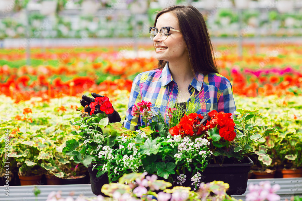 Beautiful young smiling girl in glasses, worker with flowers in greenhouse. Concept work in the greenhouse. Copy space