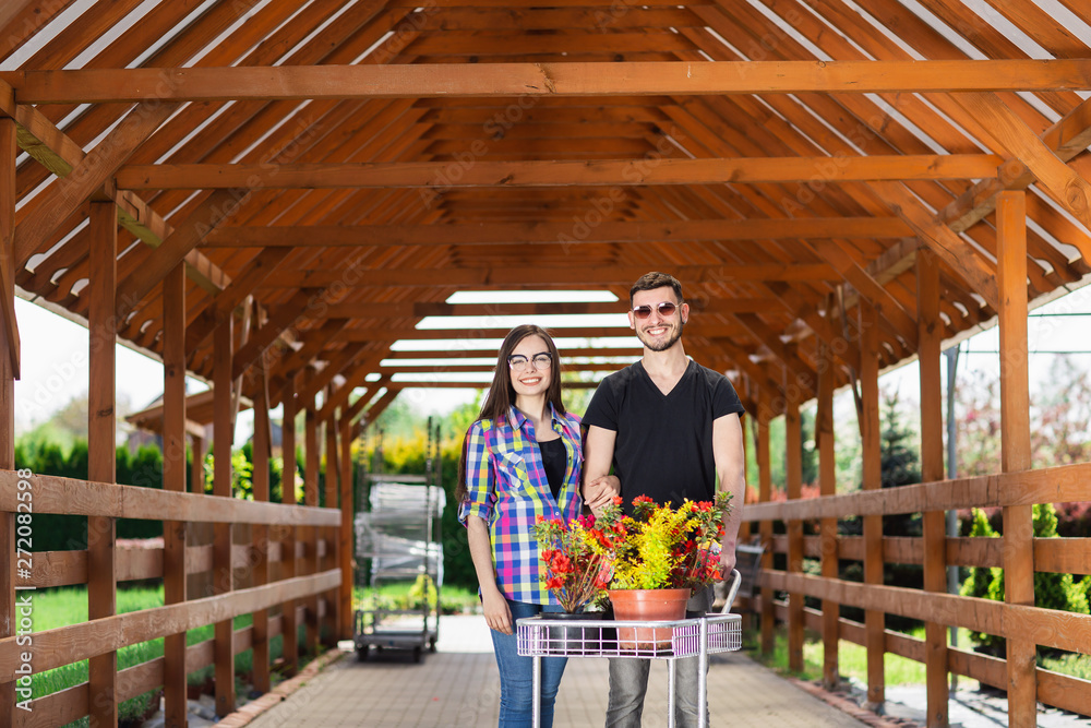 Young couple with a carriage full of different plants in the greenhouse