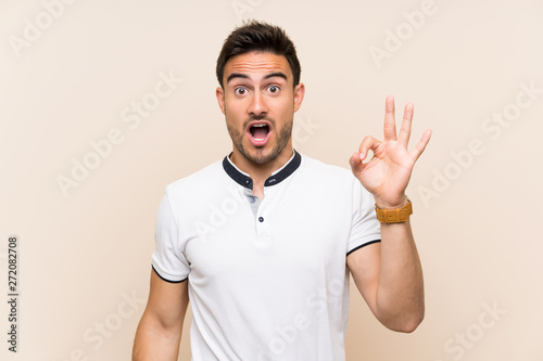 Handsome young man over isolated background surprised and showing ok sign © luismolinero