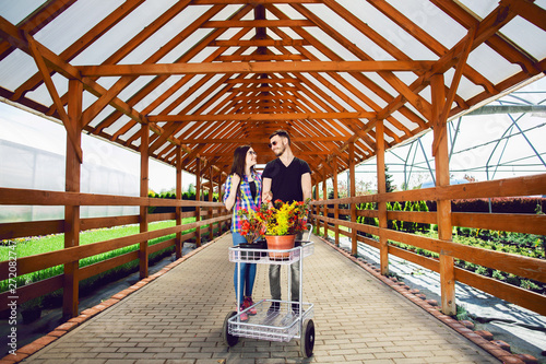 Young couple with a carriage full of different plants in the greenhouse © Olha