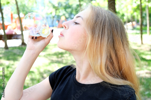 Beautiful caucasian teen girl with blond hair and freckles blowing soap bubbles outdoors.