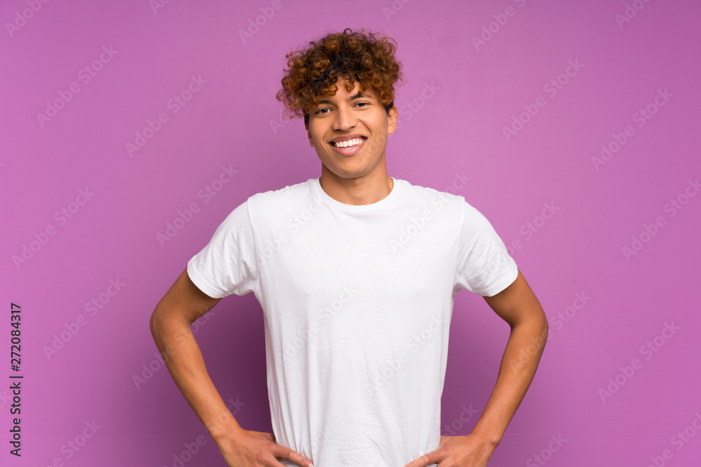 Young african american man over isolated purple wall posing with arms at hip and smiling Young african american man over isolated purple wall posing with arms at hip and smiling