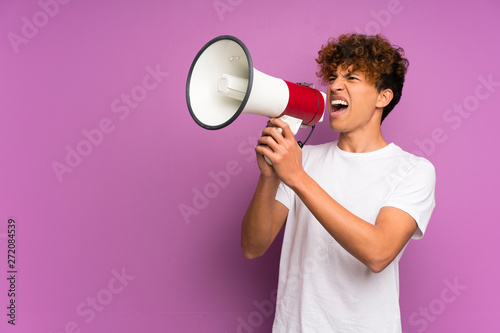 Young african american man over isolated purple wall shouting through a megaphone