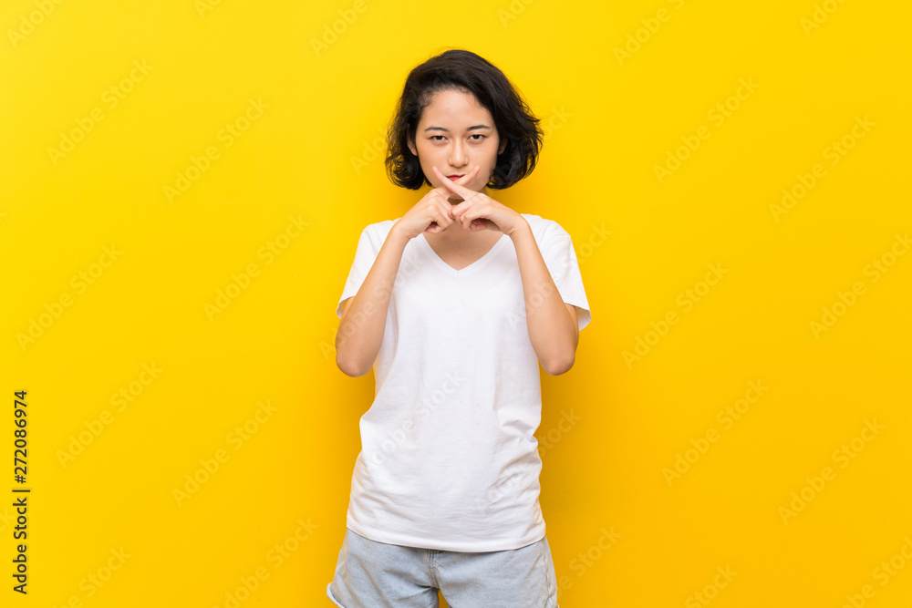 Asian young woman over isolated yellow wall showing a sign of silence gesture Asian young woman over isolated yellow wall showing a sign of silence gesture