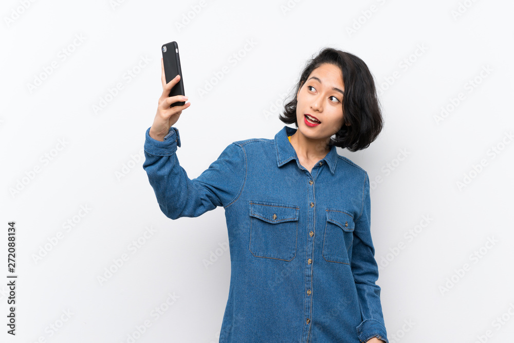 Asian young woman over isolated white background making a selfie