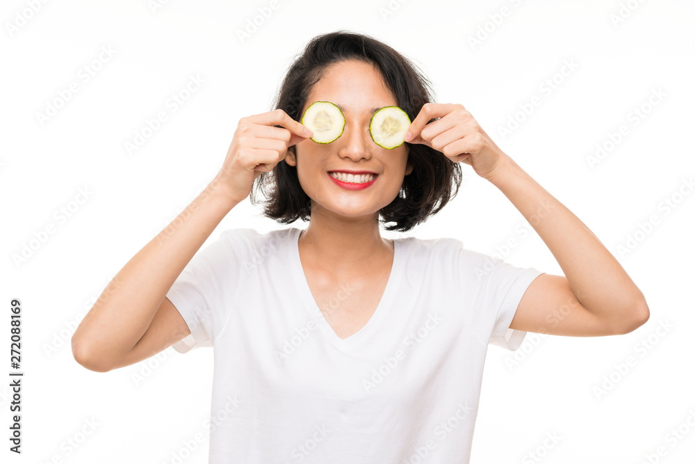 Asian young woman over isolated background holding slices of cucumber Asian young woman over isolated background holding slices of cucumber