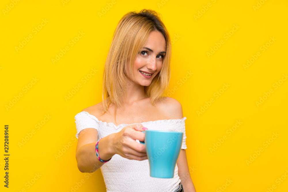 Young blonde woman over isolated yellow wall holding hot cup of coffee Young blonde woman over isolated yellow wall holding hot cup of coffee