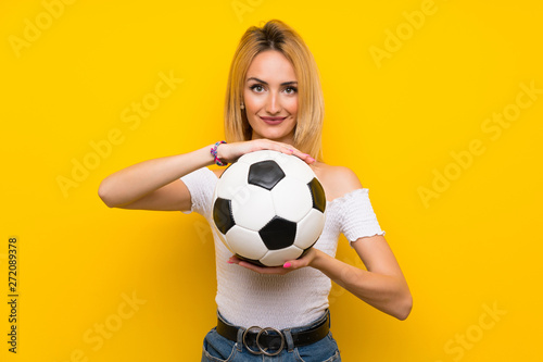 Young blonde woman over isolated yellow wall holding a soccer ball © luismolinero