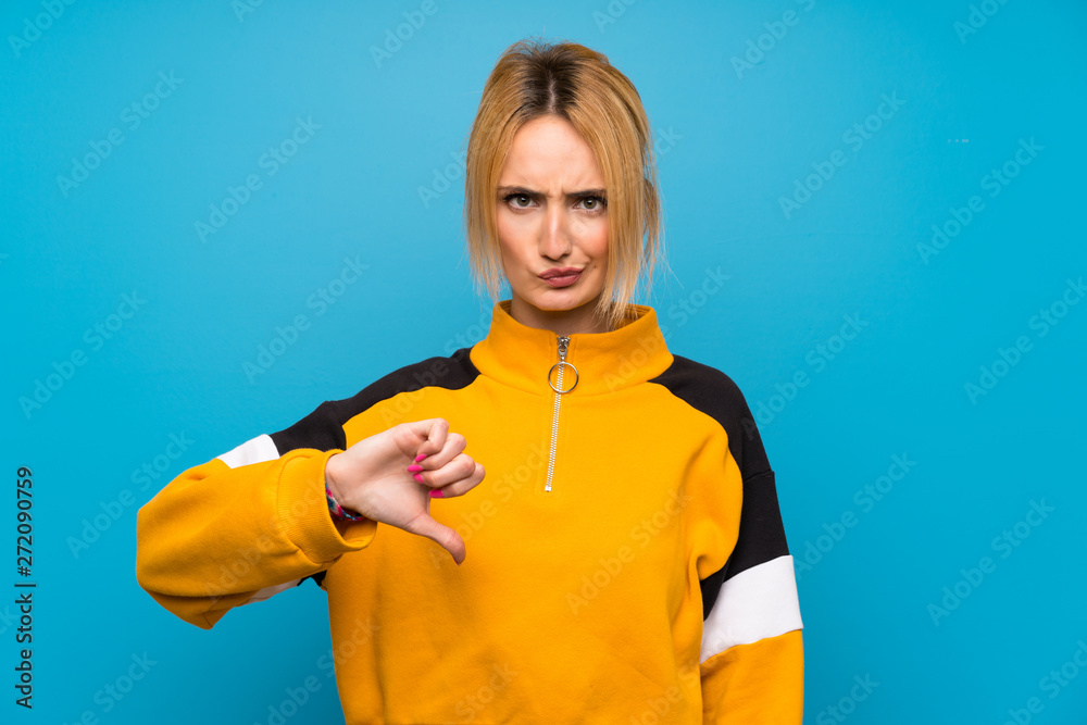 Young blonde woman over isolated blue background showing thumb down sign Young blonde woman over isolated blue background showing thumb down sign