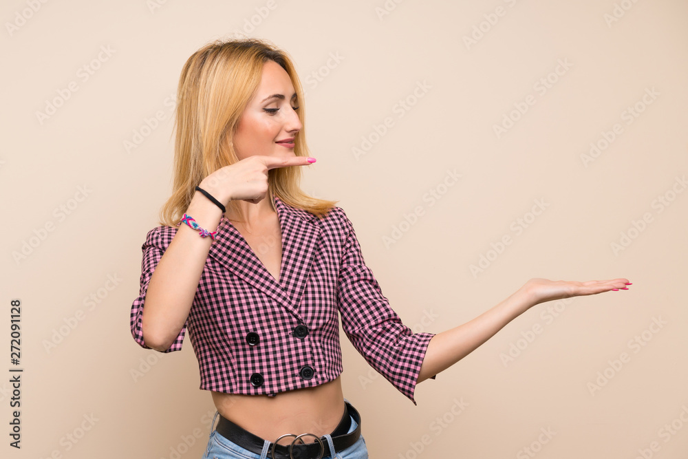 Young blonde woman with pink jacket over isolated wall holding copyspace imaginary on the palm to insert an ad Young blonde woman with pink jacket over isolated wall holding copyspace imaginary on the palm to insert an ad