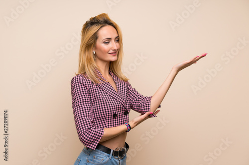 Young blonde woman with pink jacket over isolated wall extending hands to the side for inviting to come