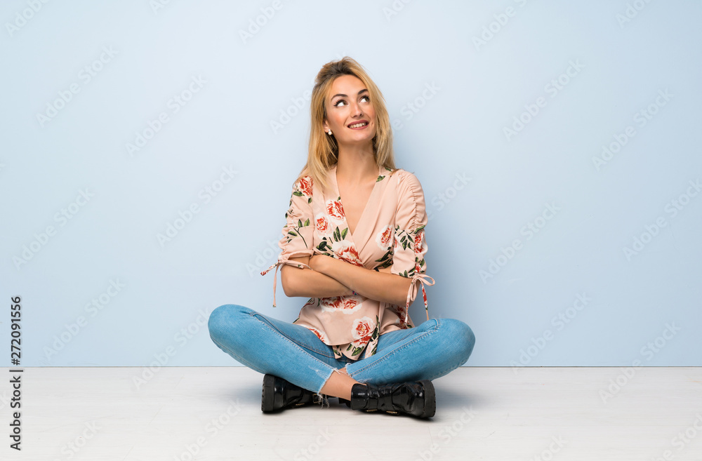 Young blonde woman sitting on the floor looking up while smiling