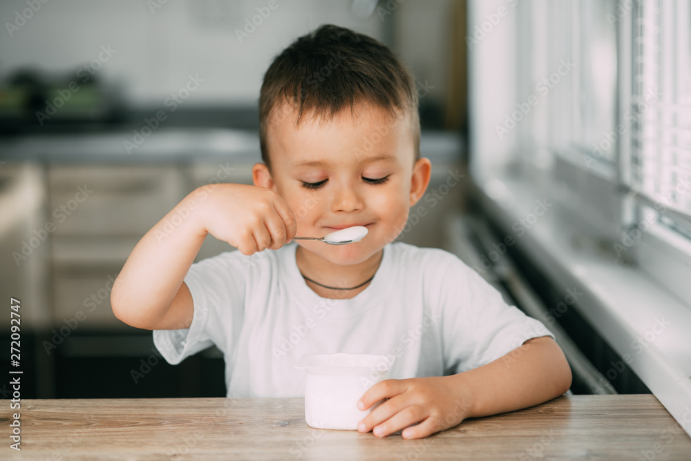 Adorable little boy eating yogurt in the kitchen in the afternoon Adorable little boy eating yogurt in the kitchen in the afternoon