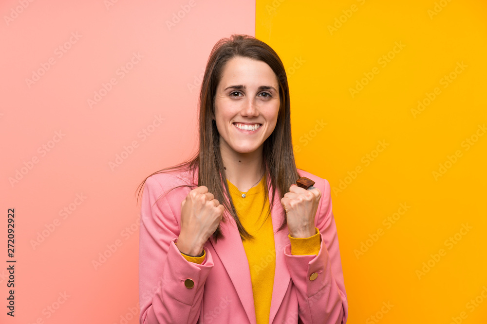 Young woman with pink suit over colorful background celebrating a victory Young woman with pink suit over colorful background celebrating a victory