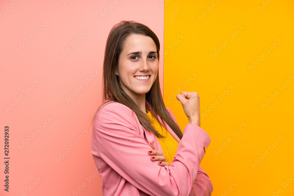 Young woman with pink suit over colorful background celebrating a victory Young woman with pink suit over colorful background celebrating a victory