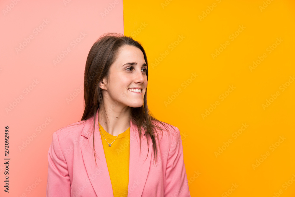 Fototapeta premium Young woman with pink suit over colorful background laughing and looking up